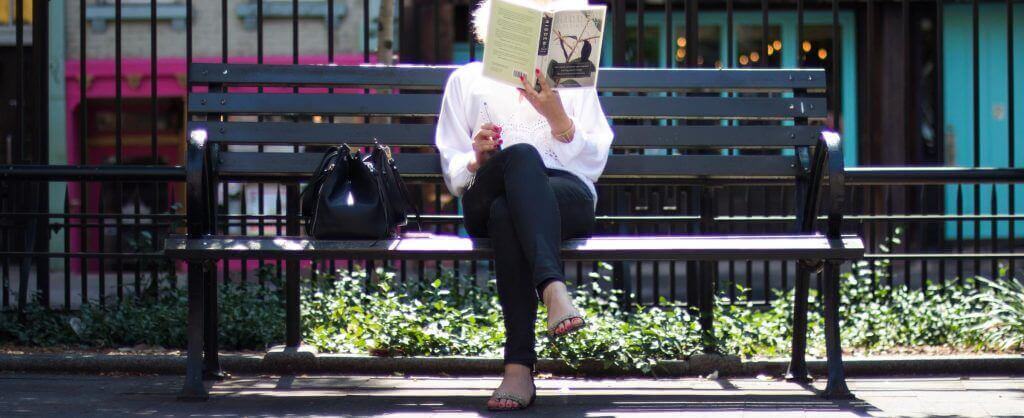 mujer leyendo un libro en un banco del parque